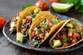 Three tacos on a plate with tomatoes, avocado and lime Royalty Free Stock Photo