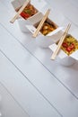 Three take away paper boxes filled with asian food placed in row on white