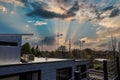 Three tall tower cranes surrounded by bare winter trees and lush green trees with blue sky and powerful clouds at sunset