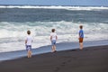 Three teen boys walk along a black volcanic beach