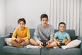 Three of the teen`s best happy friends are playing a video game at home. Three brothers play a video game, sitting on the couch, Royalty Free Stock Photo