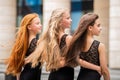 Three teenage girls with loose hair blonde redhead and brunette, stand in profile outside in summer. Vloses develop in wind