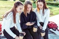 Three teenage girls schoolgirls 12-14 years old, in summer in city, in hand smartphone, cup tea drink, watch photos on Royalty Free Stock Photo