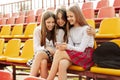 Three teenage girls watch videos together on a smartphone in the school stands. The concept of friendship and