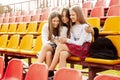 Three teenage girls watch videos together on a smartphone in the school stands. The concept of friendship and