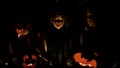 Three teenage girls in witch costumes with frightening akeup on their faces blowing out candles. Dark background