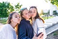 Three teenage schoolgirl girls, summer park, take pictures on smartphone, selfie on phone. Online video call to Internet