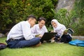 three teenagers in serious school uniforms study together using a laptop while sitting