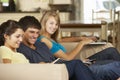 Three Teenagers Sitting On Sofa At Home Using Mobile Phone, Tablet Computer And Laptop Royalty Free Stock Photo