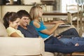 Three Teenagers Sitting On Sofa At Home Using Mobile Phone, Tablet Computer And Laptop Royalty Free Stock Photo