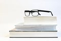 Three thick books on a table with glasses and a white background