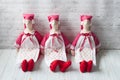 Three tilde dolls in red dresses, and white aprons, and red kalpaks sit on a light background. Interior dolls. There is a place