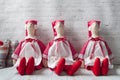 Three tilde dolls in red dresses, and white aprons, and red kalpaks sit on a light background. Interior dolls. There is a place