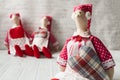 Three tilde dolls in red dresses, and white aprons, and red kalpaks sit on a light background. Interior dolls. There is a place