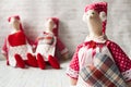 Three tilde dolls in red dresses, and white aprons, and red kalpaks sit on a light background. Interior dolls. There is a place