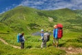 Three tourists with large backpacks stand on a trail in the Ukrainian Carpathians and look Lake Nesamovyte