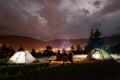 Three tourists sitting on boards around the campfire near tents