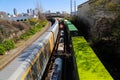 Three trains on the railroad tracks with a rusty iron bridge over the trains surrounded by lush green trees and plants Royalty Free Stock Photo