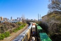 Three trains riding on the railroad tracks surrounded by lush green trees and bare winter trees and clouds, blue sky and a rainbow