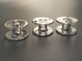 Three transparent plastic sewing machine bobbins. Textile industry. Detail of sewing equipment. Gray background, back lighting Royalty Free Stock Photo