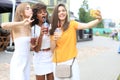 Three trendy cool hipster girls, friends drink cocktail and taking selfie in city background