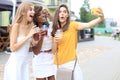 Three trendy cool hipster girls, friends drink cocktail and taking selfie in city background
