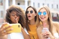 Three trendy cool hipster girls, friends drink cocktail and taking selfie in city background