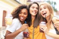 Three trendy cool hipster girls, friends drink cocktail in urban city background.