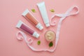 three tubes with cosmetic creams, one jar with cosmetics, green leaves, white ribbon on a pink background