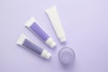 Three tubes with cosmetic creams, one jar with cosmetics on a lilac background