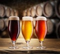 Three type of beer with foam head on wooden table. Blurred brewery cellar at the background