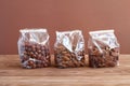 Three types of nuts - hazelnuts, almonds, pecan nuts - in transparent bags on a wooden table against a brown wall. Royalty Free Stock Photo