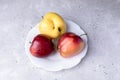 Three ugly apples on white figured plate on grey concrete background.