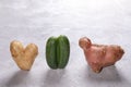 Three ugly vegetables: potato and cucumber on grey concrete background.