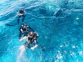 Three underwater divers in black scuba diving suits, a man and a woman with oxygen bottles sink under the transparent blue water i