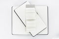 Three unfold black notebooks lie on top of each other. Fan open notepad with blank pages. White back. Top view