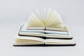 Three unfold notebooks lie on top of each other and fan open notepad with blank light beige pages. Pyramid of books. White back