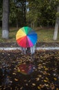 three unrecognizable children hid behind large rainbow-colored umbrella. Reflection in puddle Royalty Free Stock Photo