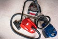 Three vacuum cleaners in different colors sitting on a white carpet floor. Royalty Free Stock Photo
