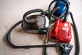 Three vacuum cleaners in different colors sitting on a white carpet floor. Royalty Free Stock Photo