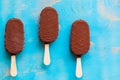Three vanilla ice cream bars with chocolate coating on rustic bl