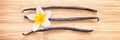 Three vanilla pods with a flower aligned on wood panoramic background Royalty Free Stock Photo