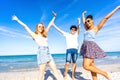 Three very happy friends having fun at the beach posing laughing looking at camera for a portrait with raised arms. Gen z