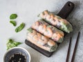 Three Vietnamese spring rolls - carrots, cucumber, corn salad, red cabbage, herbs and shrimps on a wood dark board. Soy sauce with