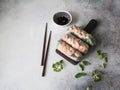 Three Vietnamese spring rolls - carrots, cucumber, corn salad, red cabbage, herbs and shrimps on a wood dark board. Soy sauce with