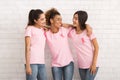 Three Volunteers In Breast Cancer T-Shirts Embracing Over White Wall