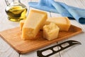 Three wedges of traditional italian hard cheese Grana Padano or Parmesan and cheese knife on a wood cutting boad near olive oil