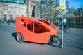 Three wheel orange vehicle in a city.