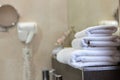 Three white bath towels are stacked on a bathroom shelf. A vase of flowers and a hairdryer are out of focus.Hotel business concept Royalty Free Stock Photo