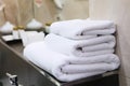 Three white bath towels are stacked on a bathroom shelf. A vase of flowers is out of focus. Hotel business concept Royalty Free Stock Photo